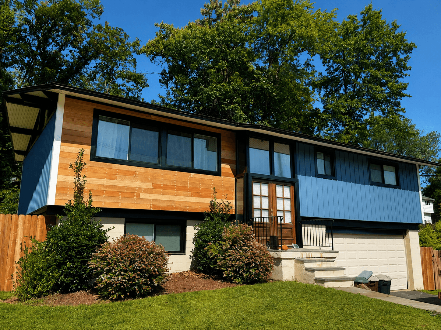 Renovated split-level exterior combining a natural wood accent panel with blue vertical board-and-batten siding and dark window frames.