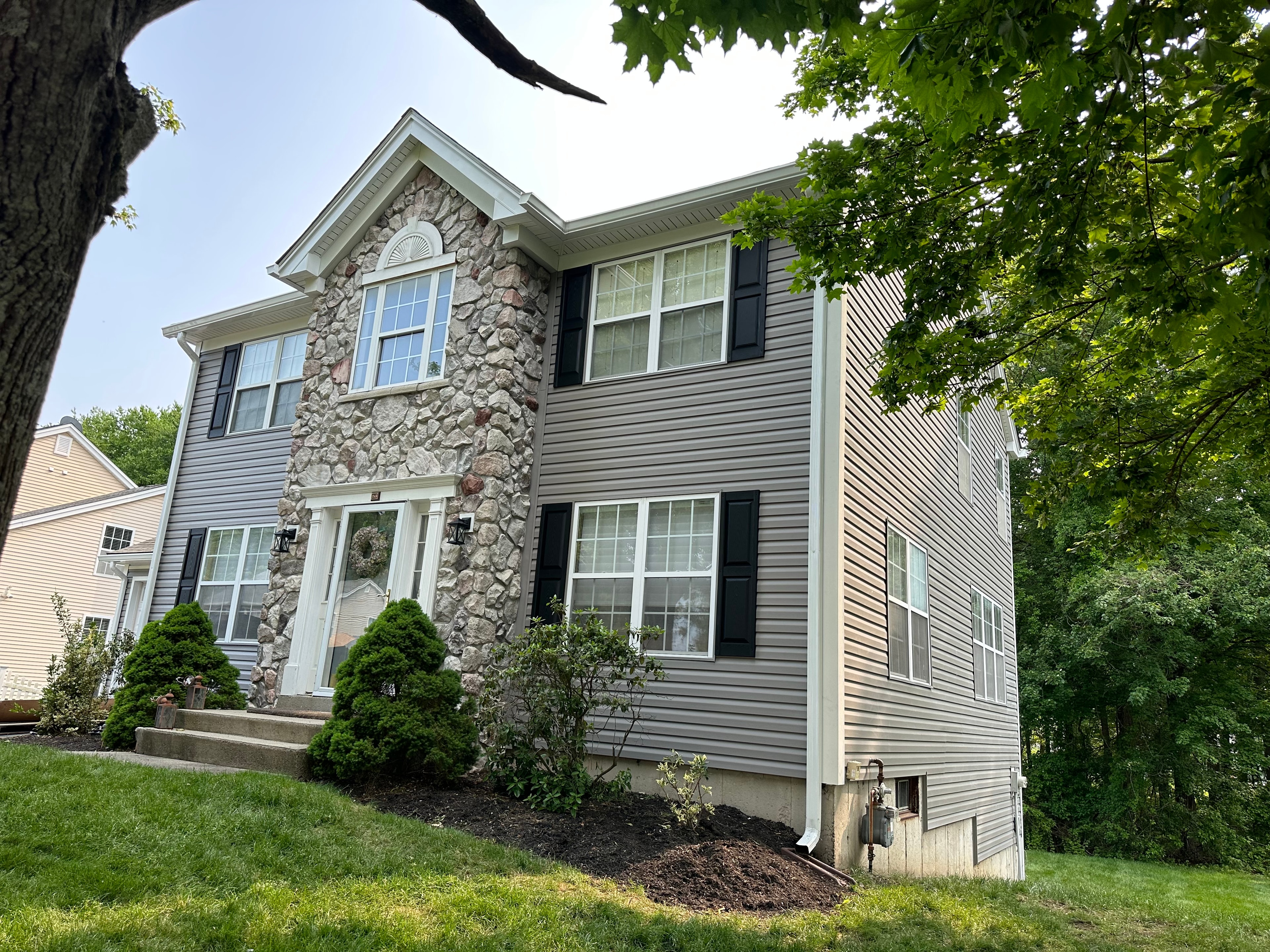 Gray horizontal siding with a full-height stone-veneer accent around the entry, black shutters and a covered stoop.