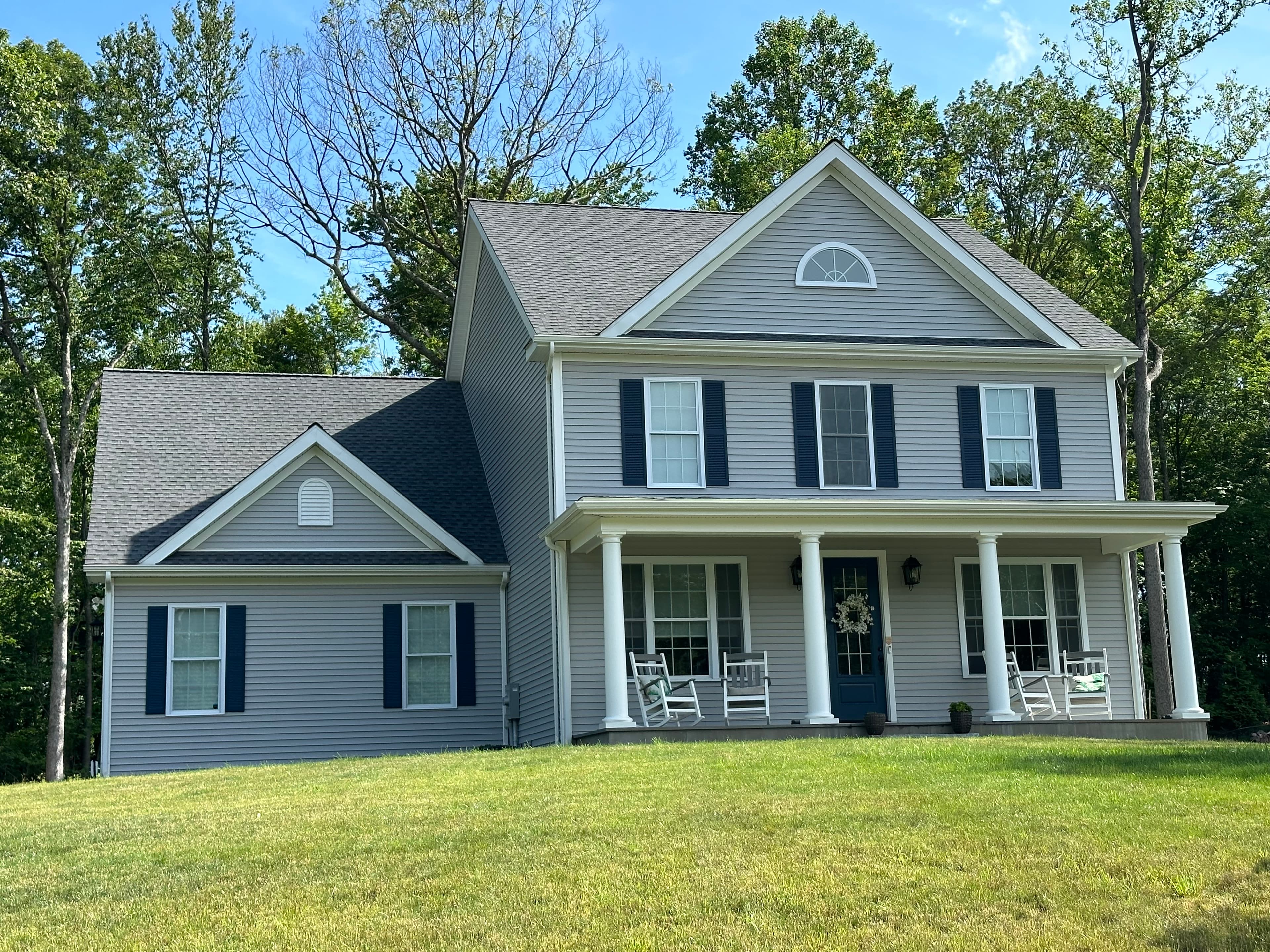 Light gray horizontal siding with black shutters, white trim, a columned covered porch and a half-round gable vent.